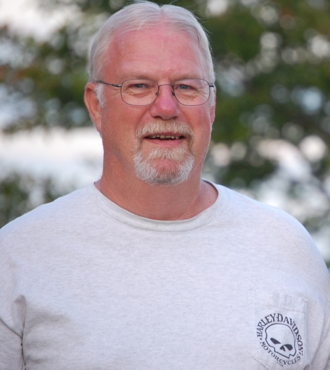 Russell Buss, wearing a heather gray tee with trees in the background, smiles at the camera.