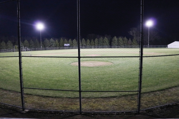 The baseball diamond at North Iowa is lit up at night with the overhead lights.
