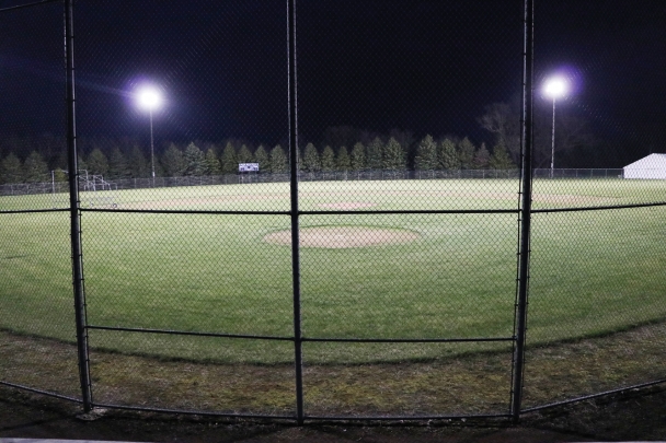 The baseball diamond at North Iowa is lit up at night with the overhead lights.