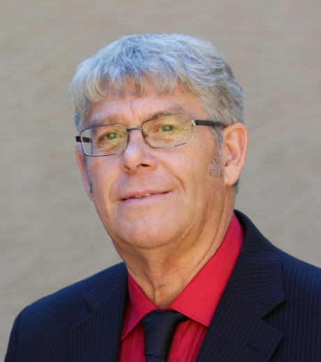 Jeffery Blome smiles at the camera, wearing a suit, tie, and glasses.