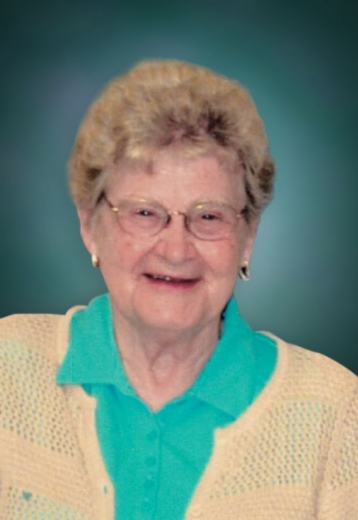 Shirley smiles with her mouth open. She wears a teal blouse with a light orange cardigan.