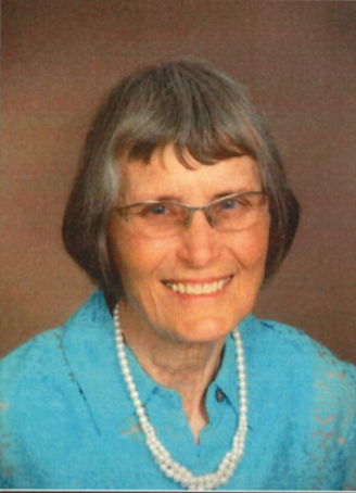 A professional portrait of Joan. She wears a blue button-up, glasses and pearl necklace.