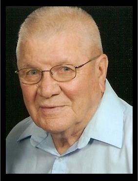 Grant Ostrander wears a light blue button-up in front of a black background while smiling at the camera.