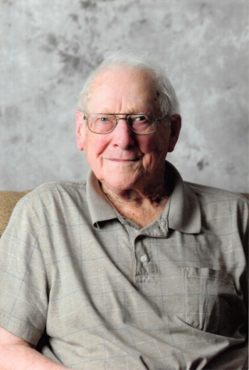 Jake wears a greige polo shirt as he sits with a pleasant expression in front of a mottled background.